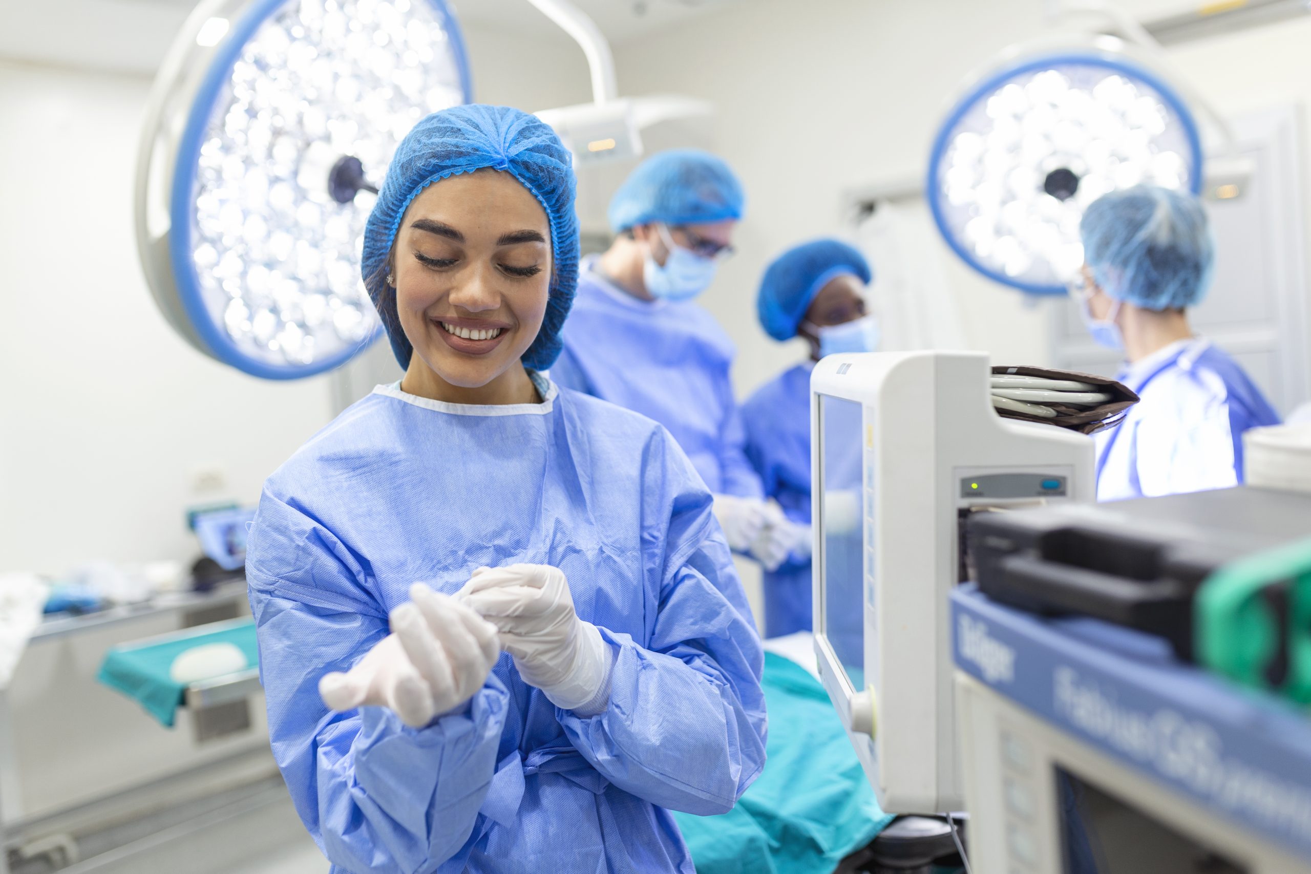 Portrait of beautiful female doctor surgeon putting on medical gloves standing in operation room. Surgeon at modern operating room